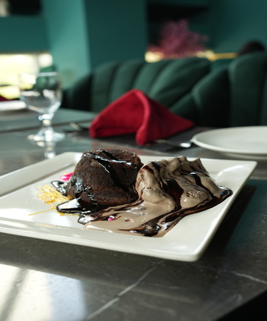 Indulgent molten lava cake with a gooey chocolate center, served warm with a scoop of vanilla ice cream and a sprinkle of cocoa. Savor this exquisite dessert at De Flambe, a top-rated restaurant in G8 Islamabad, perfect for a romantic dinner or a sweet treat after a meal.